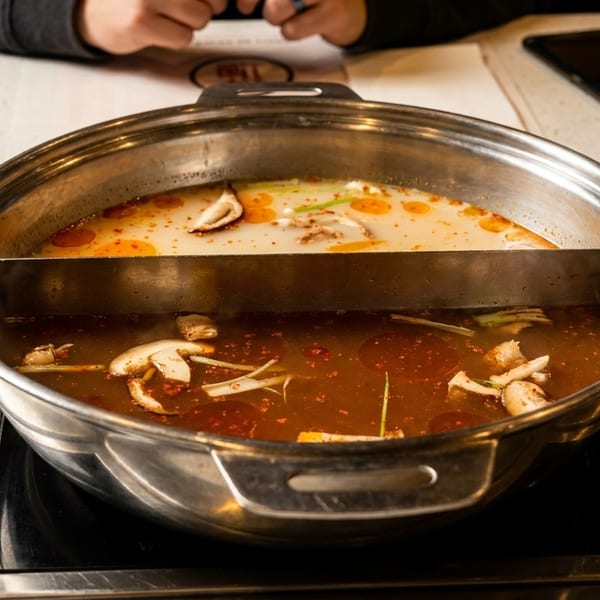 A hot pot with two broths, one spicy red and one creamy white, simmering on a burner.