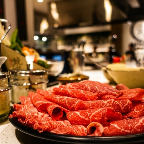 Platter of thinly sliced raw beef with marbling, with condiments and a chef in the background.
