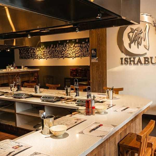 Interior of Ishabu restaurant with a long counter, cooking stations, and wooden chairs.