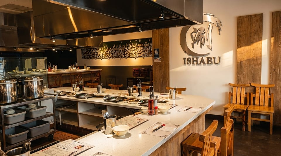 Interior of Ishabu restaurant with a long counter, cooking stations, and wooden chairs.